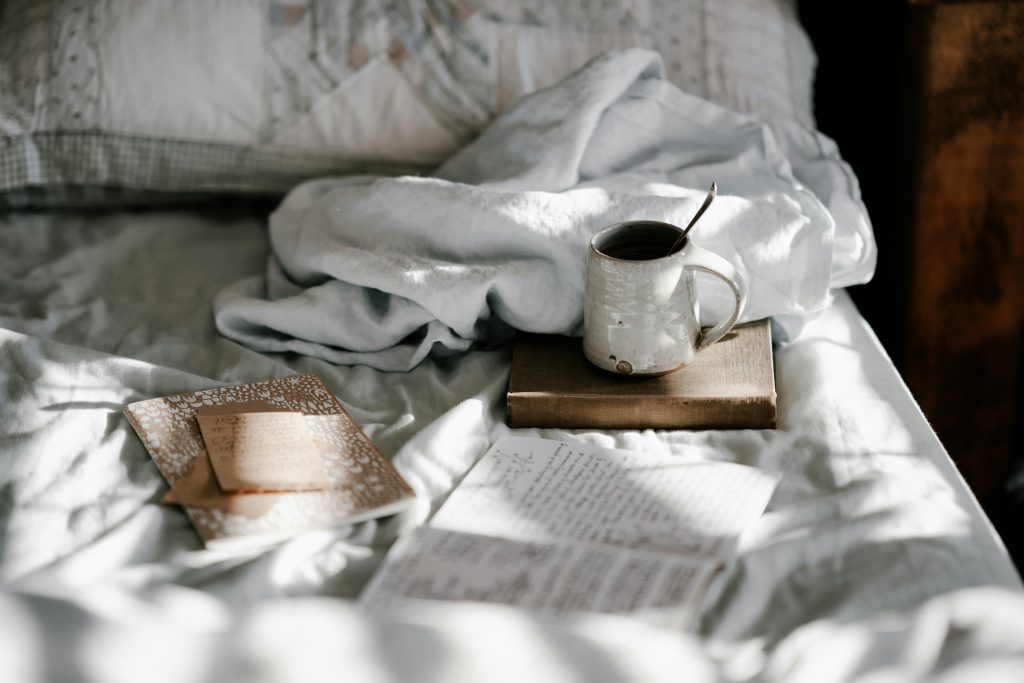 cozy bed with white sheet a mug and books